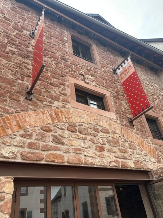 Façade en grès du Refuge fortifié avec deux bannières rouges